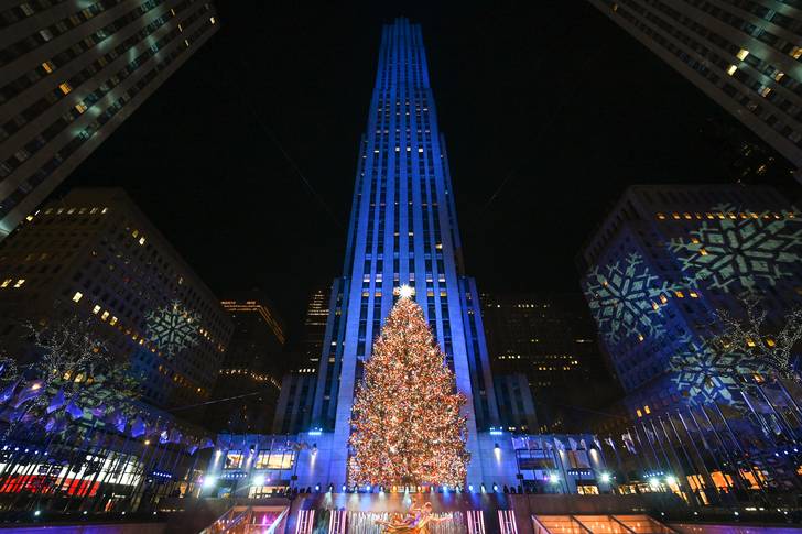 The Rockefeller Center tree is lit in multi-colored lights, within Rockefeller Center buildings